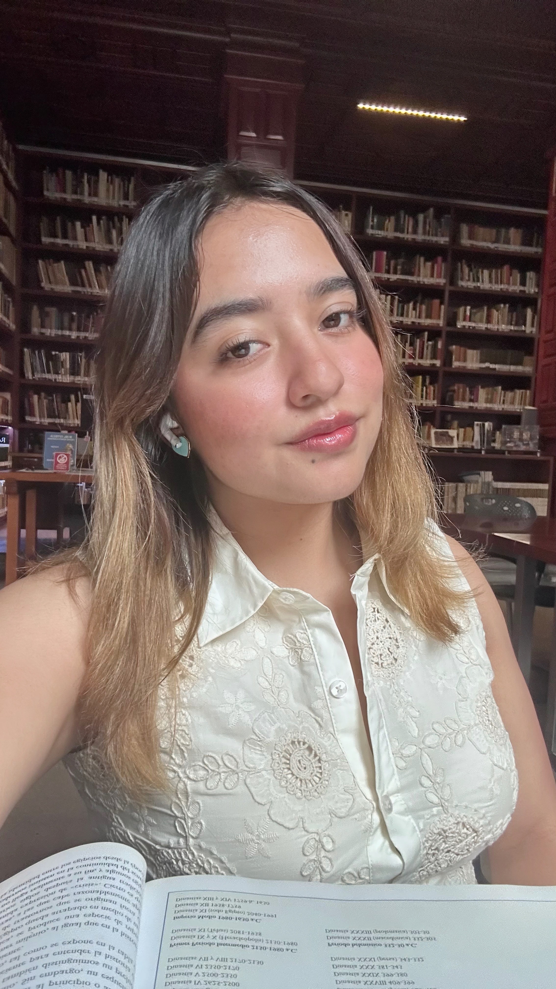 Nataly Melo en una biblioteca, con un libro abierto, frente a estanterías de madera.